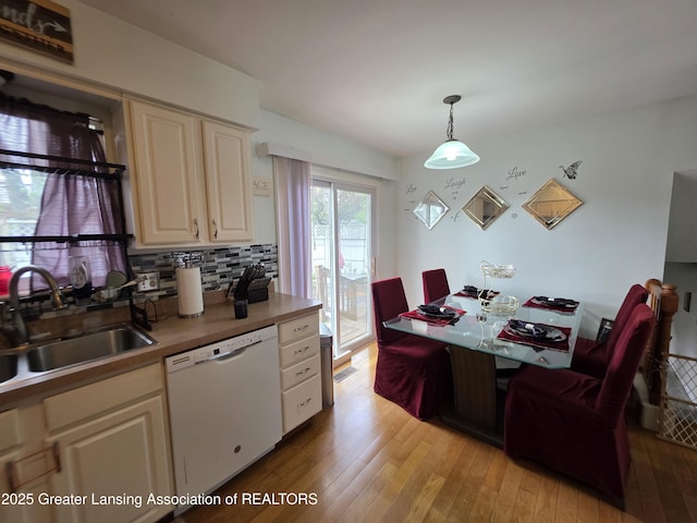 kitchen featuring dishwasher, a sink, light wood-style flooring, backsplash, and pendant lighting