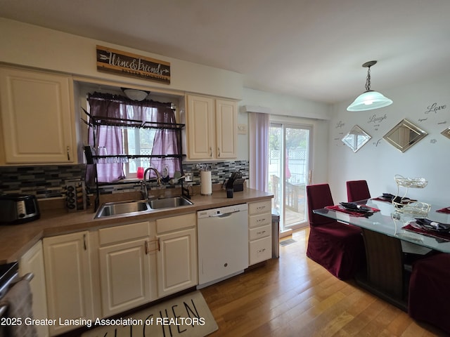 kitchen with dishwasher, a sink, backsplash, light wood-style flooring, and hanging light fixtures