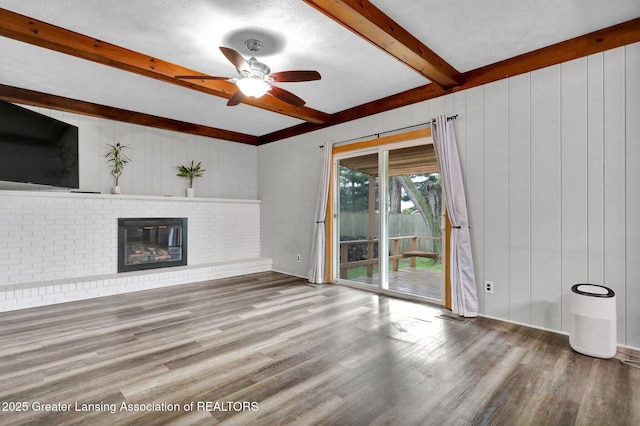 910 Pecos Dr, Lansing, MI 48917 - unfurnished living room featuring beam ceiling, wood finished floors, ceiling fan, a brick fireplace, and wooden walls