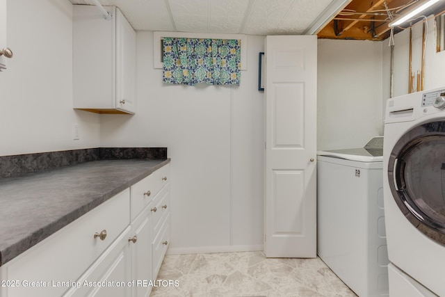 clothes washing area with washing machine and dryer, cabinet space, and baseboards