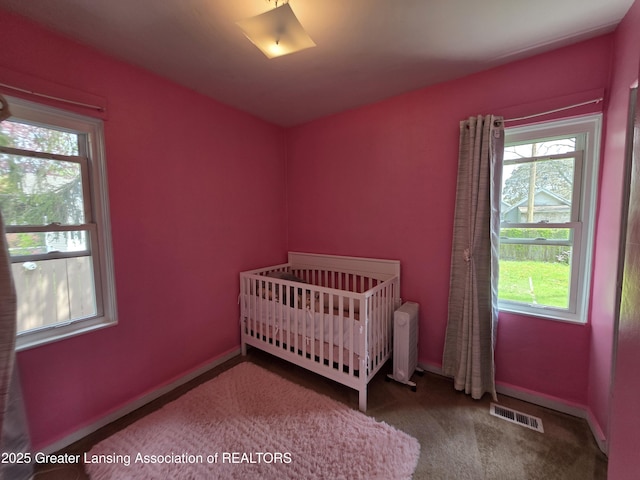 carpeted bedroom featuring multiple windows, a crib, baseboards, and radiator