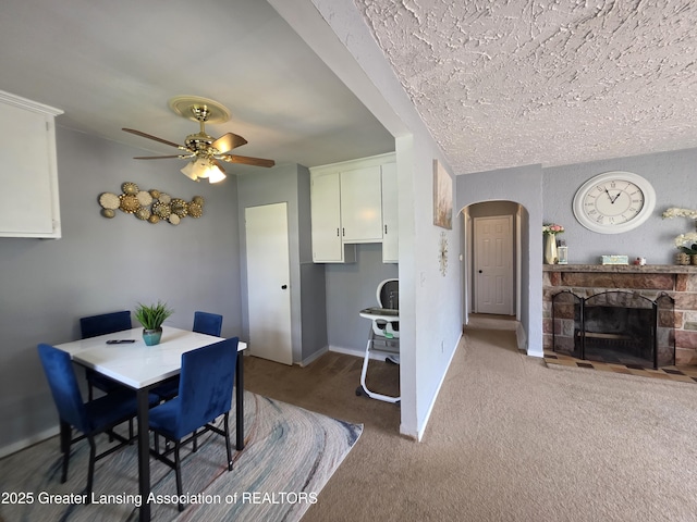 carpeted dining area with a fireplace, a ceiling fan, arched walkways, and baseboards