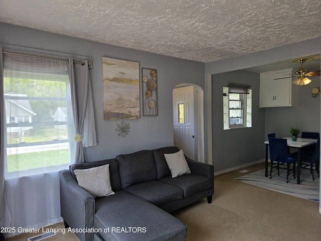 living area featuring arched walkways, a textured ceiling, carpet floors, and ceiling fan