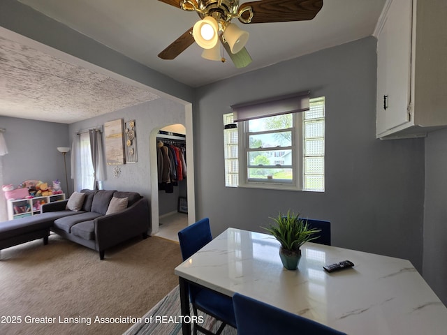 carpeted dining area featuring arched walkways, a ceiling fan, and a textured ceiling