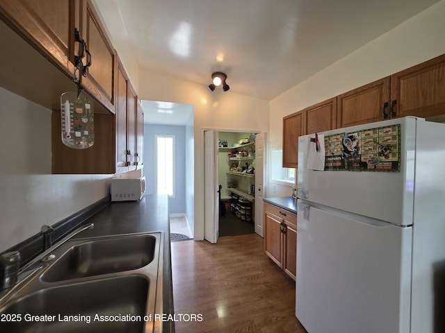 kitchen featuring white appliances, a sink, brown cabinetry, and dark wood finished floors