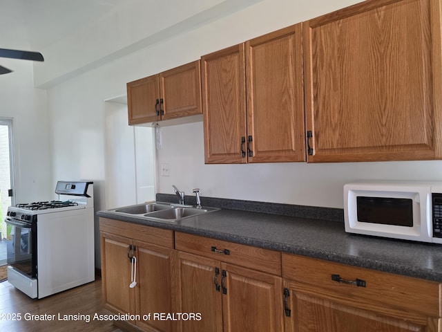 kitchen featuring gas stove, white microwave, a sink, dark countertops, and brown cabinets