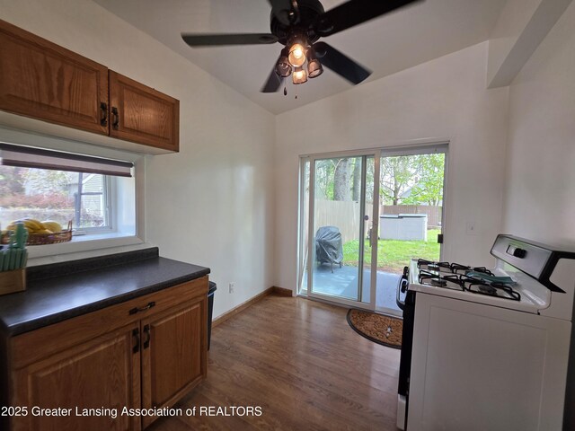 kitchen featuring white range with gas stovetop, dark countertops, lofted ceiling, a ceiling fan, and dark wood-style floors