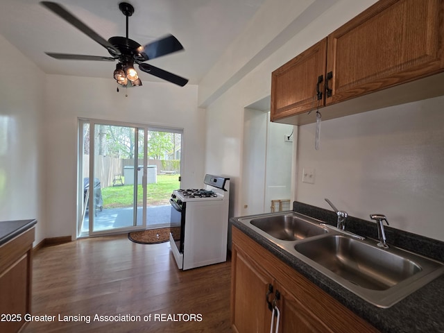 kitchen with white range with gas cooktop, a sink, dark countertops, and dark wood-style floors
