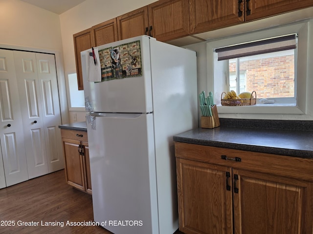 kitchen featuring freestanding refrigerator, dark countertops, brown cabinets, and dark wood-style flooring