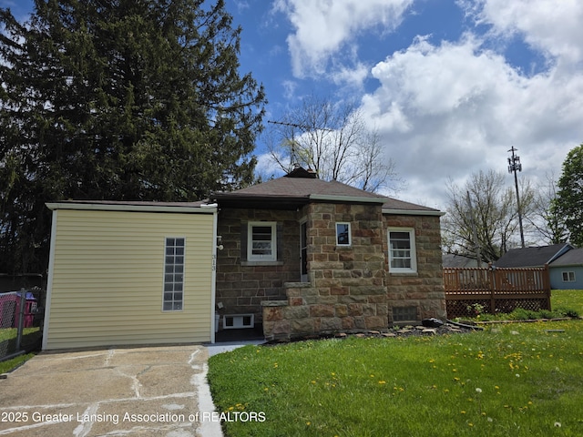 rear view of house with stone siding, a wooden deck, a yard, and a chimney