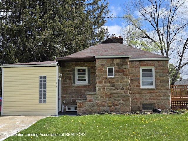 back of house featuring stone siding, a chimney, a lawn, and a shingled roof