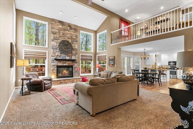 living room with high vaulted ceiling, plenty of natural light, a stone fireplace, recessed lighting, and a chandelier