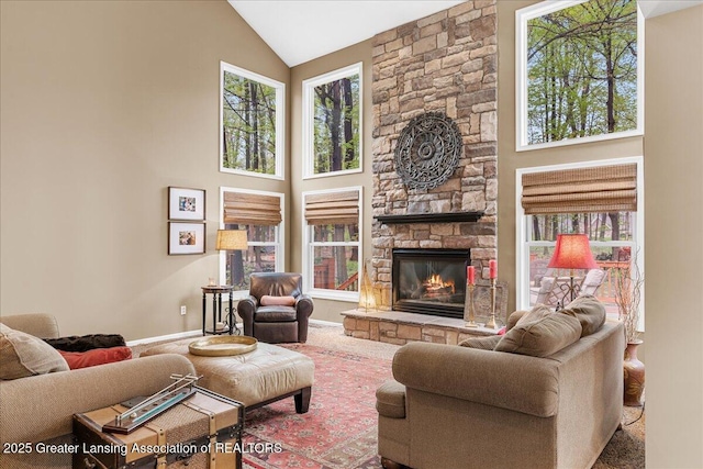 carpeted living room featuring a stone fireplace, baseboards, and high vaulted ceiling