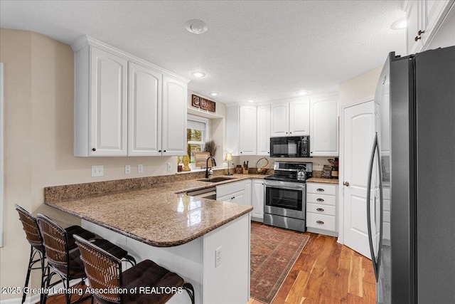 kitchen with stainless steel appliances, a peninsula, a sink, light wood finished floors, and white cabinets