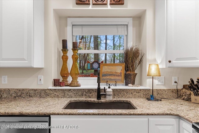 kitchen view of stainless steel dishwasher, a sink, white cabinetry, and light stone countertops