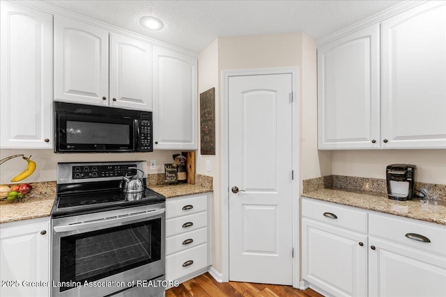 kitchen featuring black microwave, stainless steel electric range oven, white cabinets, light stone countertops, and a textured ceiling