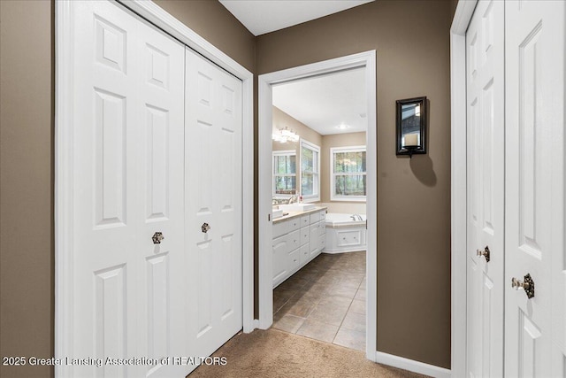 corridor with light carpet, light tile patterned floors, baseboards, and a sink