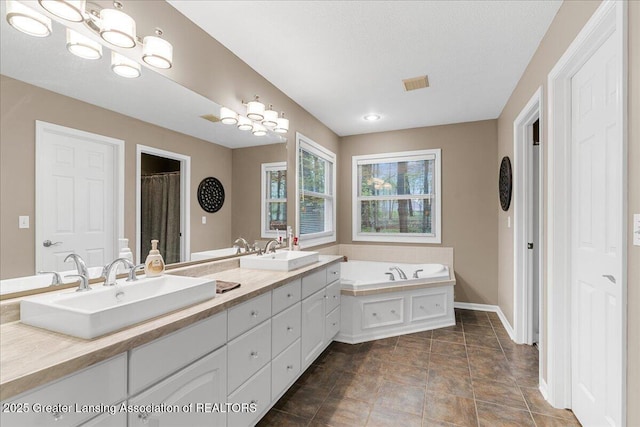full bath featuring double vanity, a bath, baseboards, a chandelier, and a textured ceiling