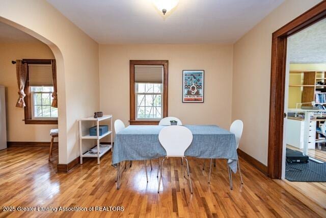 dining space with wood finished floors, arched walkways, and baseboards