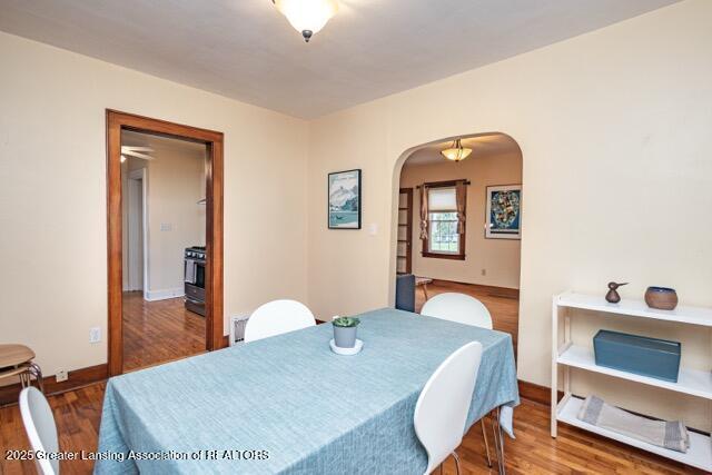dining space featuring arched walkways, wood finished floors, and baseboards