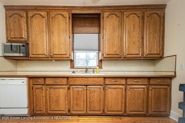 kitchen with stainless steel microwave, dishwasher, brown cabinetry, and a sink