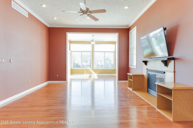 unfurnished living room featuring ceiling fan, crown molding, light wood-style flooring, a glass covered fireplace, and baseboards