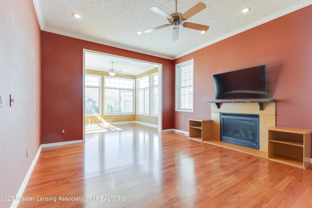 unfurnished living room with a ceiling fan, wood finished floors, a glass covered fireplace, a textured ceiling, and crown molding