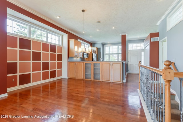 interior space featuring crown molding, wood finished floors, a peninsula, recessed lighting, and hanging light fixtures