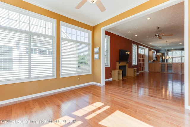 unfurnished living room featuring ceiling fan, light wood-style flooring, crown molding, and baseboards