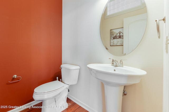 half bathroom featuring toilet, wood finished floors, and baseboards