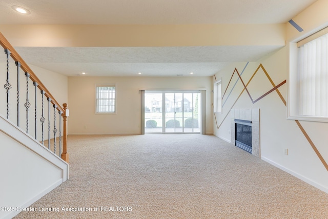 unfurnished living room featuring carpet flooring, baseboards, a tiled fireplace, stairs, and recessed lighting