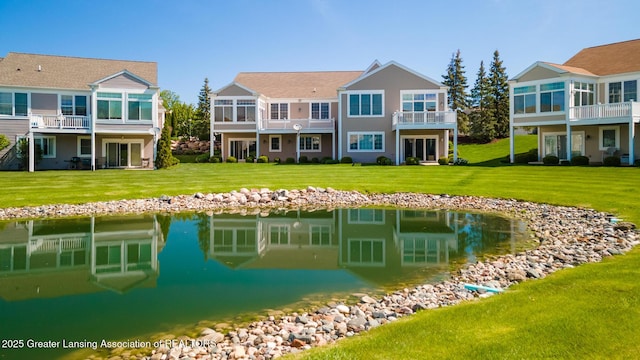 rear view of house with a lawn, a water view, and a balcony