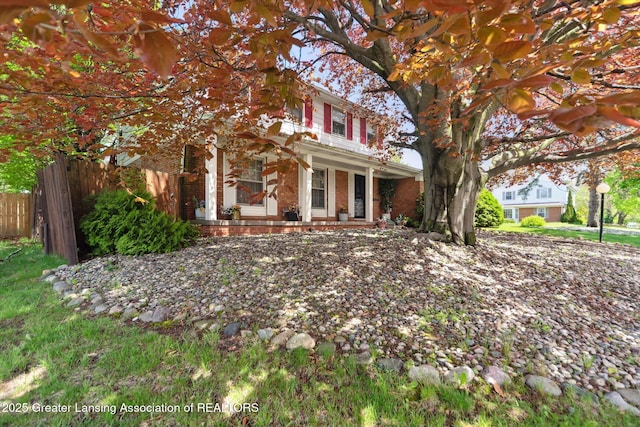 obstructed view of property featuring brick siding, fence, and covered porch