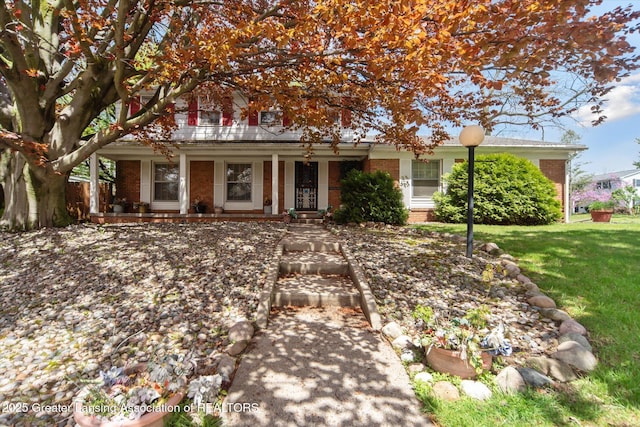 view of property hidden behind natural elements featuring brick siding, a front yard, and a porch