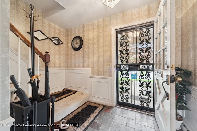 entrance foyer with wallpapered walls, stone tile flooring, and wainscoting