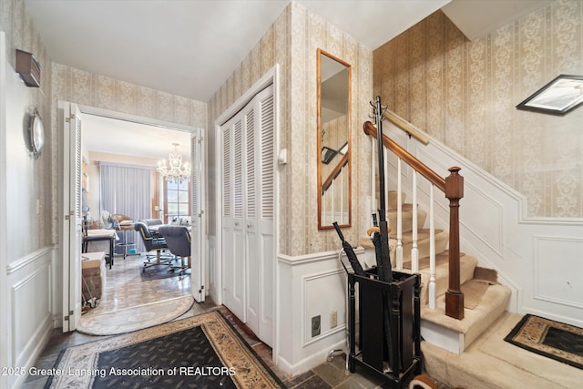 corridor featuring wallpapered walls, a decorative wall, a chandelier, and stairs