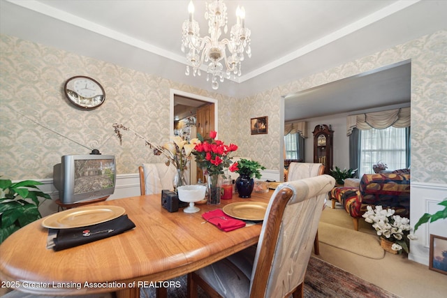 carpeted dining space featuring wallpapered walls, a chandelier, and wainscoting