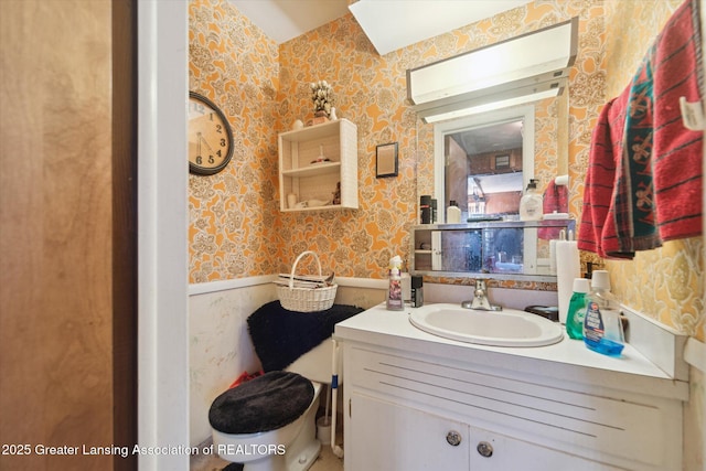 bathroom featuring wallpapered walls, a wainscoted wall, vanity, and toilet
