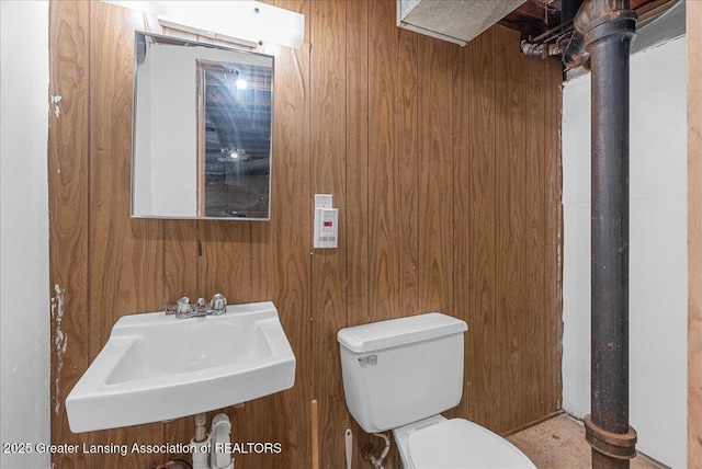 half bath with wooden walls, toilet, and a sink