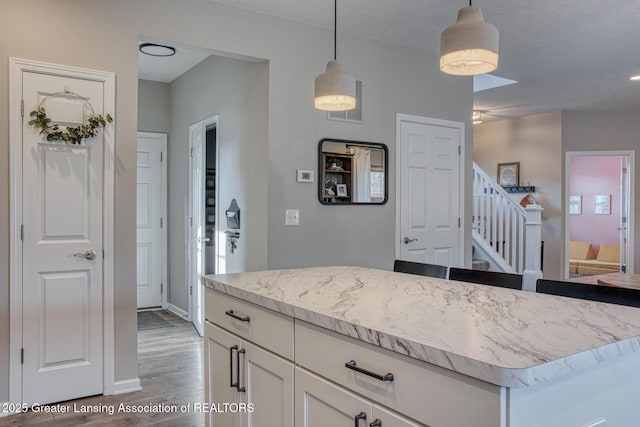 kitchen featuring hanging light fixtures, white cabinetry, wood finished floors, a kitchen island, and light stone countertops