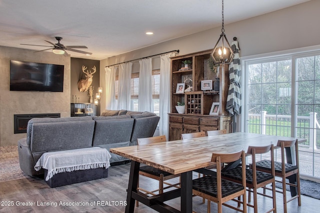 dining space with wood finished floors, a ceiling fan, a fireplace, and a chandelier