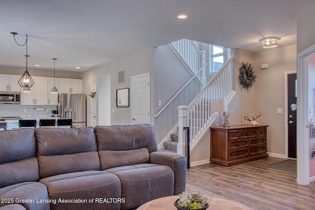 living room featuring stairs, a textured ceiling, light wood-type flooring, baseboards, and recessed lighting