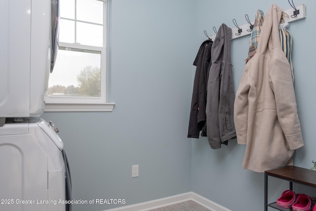 clothes washing area with stacked washing machine and dryer and baseboards