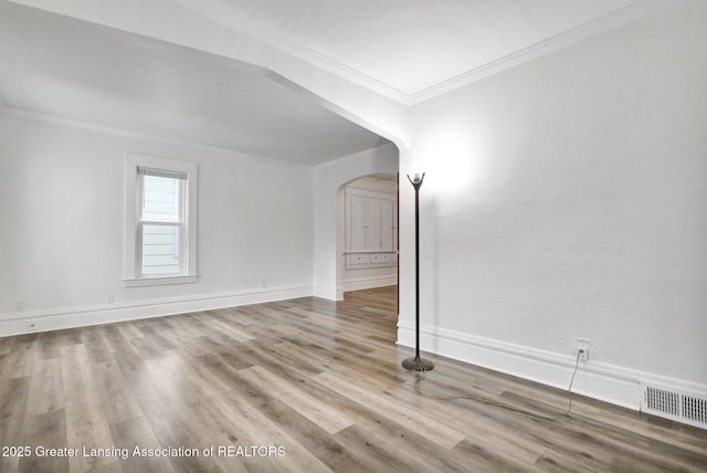 unfurnished living room with arched walkways, ornamental molding, wood finished floors, and baseboards