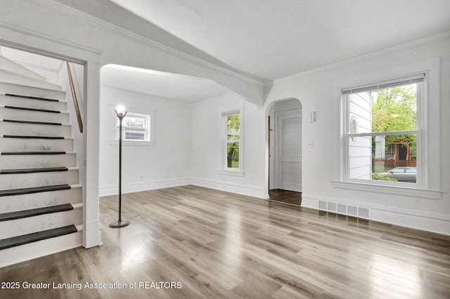 unfurnished living room with crown molding, wood finished floors, stairway, arched walkways, and baseboards