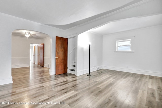 unfurnished room featuring arched walkways, ornamental molding, wood finished floors, a ceiling fan, and baseboards