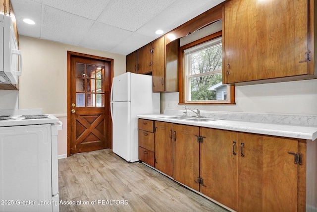 kitchen with white appliances, a sink, light wood-style flooring, brown cabinets, and light countertops