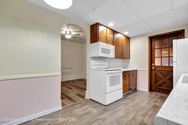 kitchen with white appliances, light countertops, light wood-type flooring, baseboards, and arched walkways