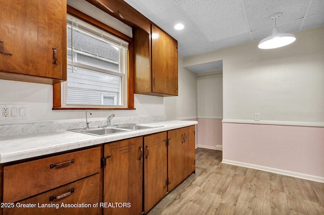 kitchen with a sink, brown cabinets, light countertops, light wood-style flooring, and baseboards