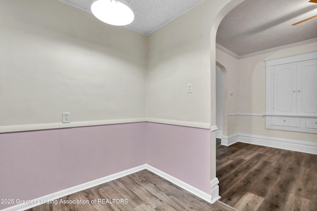 unfurnished room featuring arched walkways, wood finished floors, ceiling fan, baseboards, and crown molding